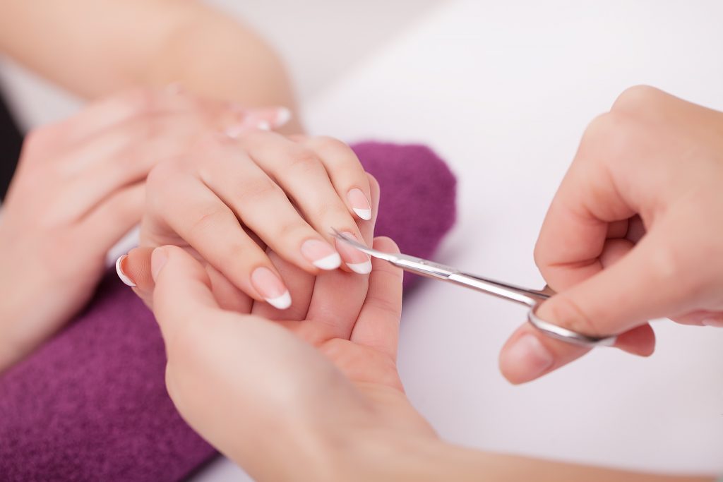 Nahaufnahme einer Frau im Nagelstudio, die von einer Kosmetikerin eine Maniküre erhält, bei der eine Schere verwendet wird