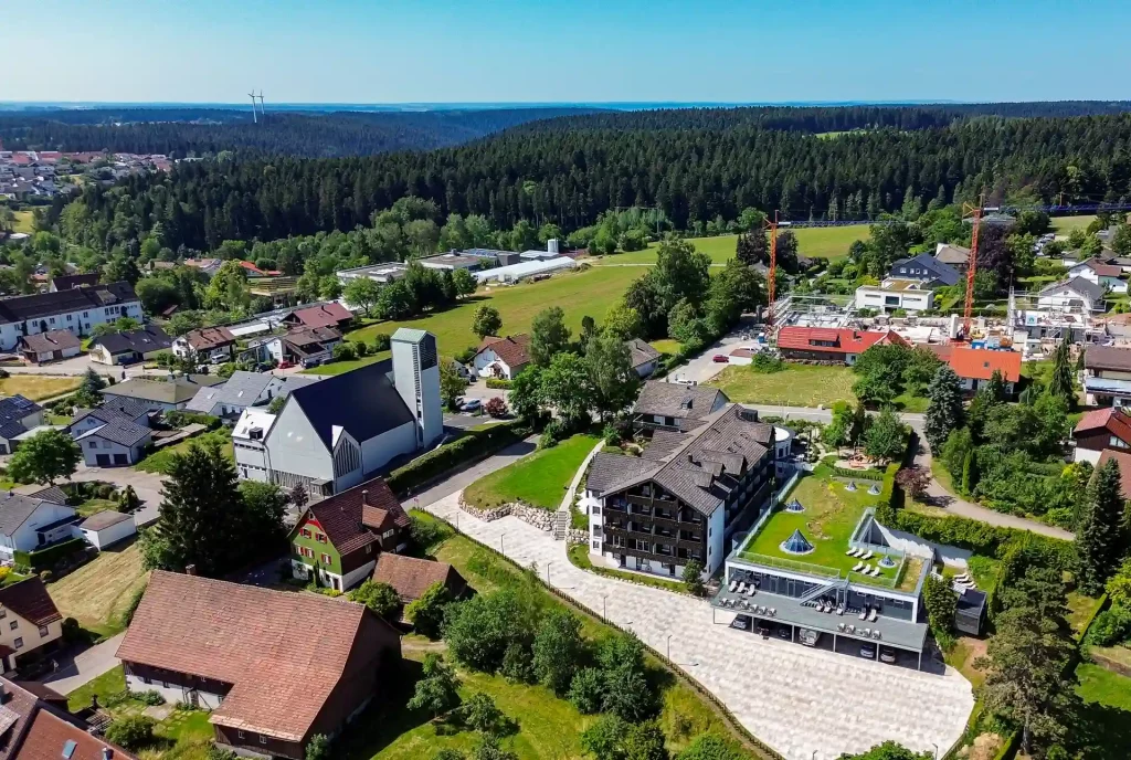 Luftbild des Wellnesshotel Hohenrodt mit Hotelgebäude, Schwarzwald und Kinzigquelle im Hintergrund