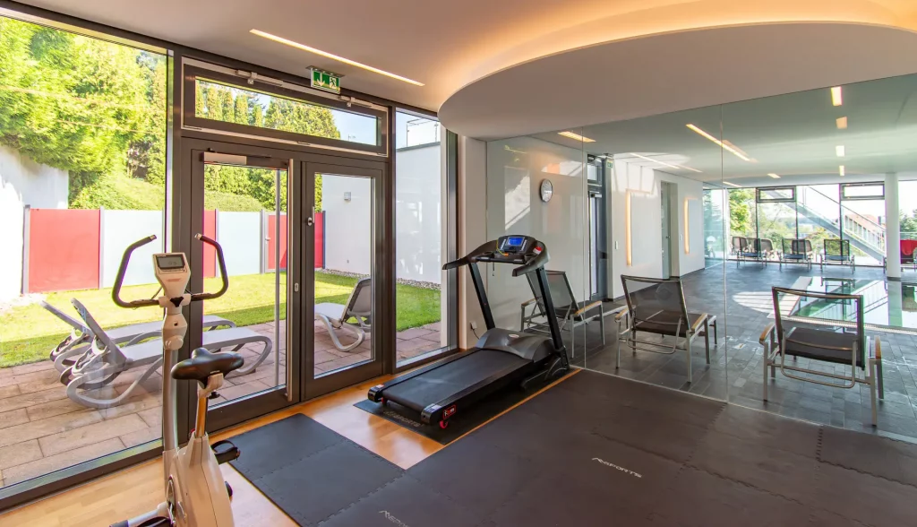 Wellness-Fitnessraum im Wellnesshotel Hohenrodt mit Blick auf den Poolbereich und große Fensterfront