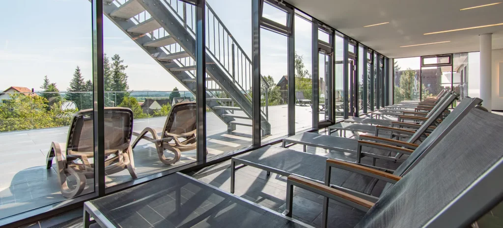 Wellnesspoolbereich im Wellnesshotel Hohenrodt mit Liegen, großer Fensterfront und Blick auf die Landschaft
